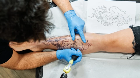 Top view of an unrecognizable tattoo artist tattooing an octopus design on his client’s leg.