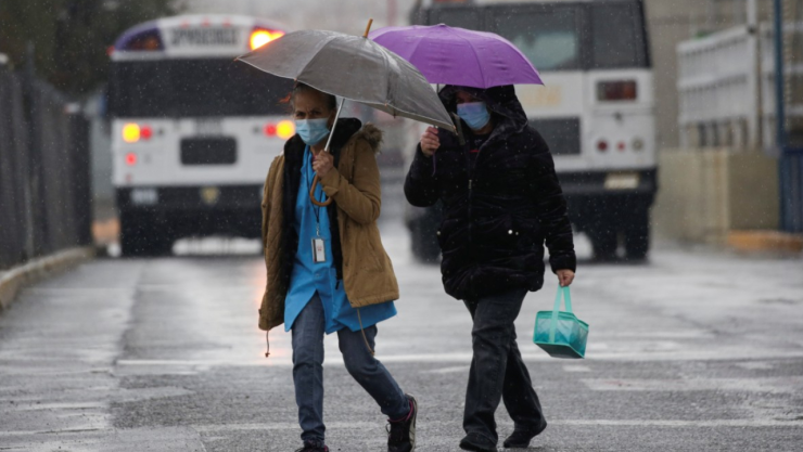 Dos mujeres muy bien abrigadas por el frío y cubriéndose con un paraguas de la lluvia.