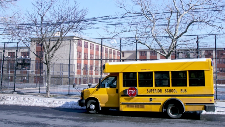 Un bus escolar amarillo, estacionado afuera de la escuela en Nueva York, en invierno, con las veredas nevadas