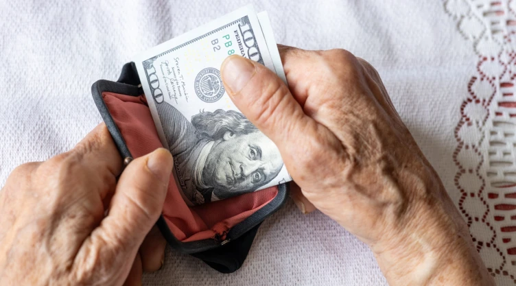 Una mujer guarda billetes de 100 dólares en su billetera.