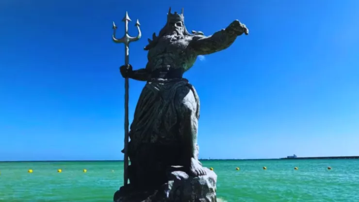 Es un hombre de barba larga apuntando hacía el lado derecho con un tridente en la mano y una corona sobre su cabeza