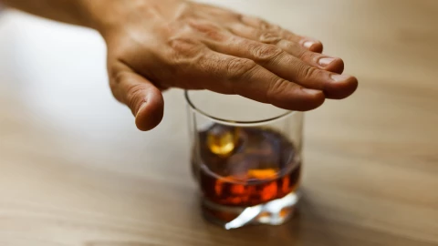 Un vaso con un tipo de bebida alcohólica y una mano encima.