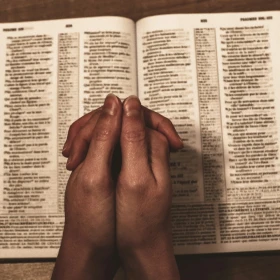 Manos orando sobre biblia abierta.
