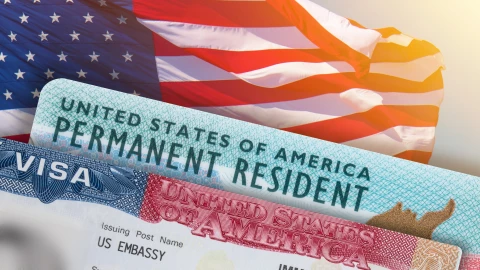 Una Green Card y una visa estadounidense sobre una bandera.