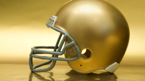 Shiny golden American football helmet on golden surface