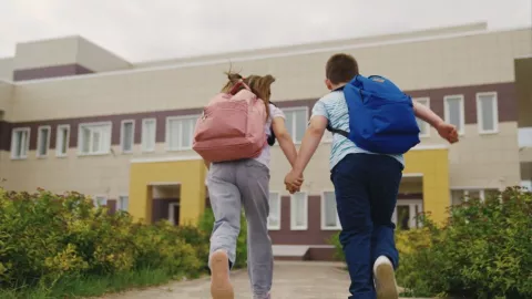 Dos niños corren hacia una escuela.