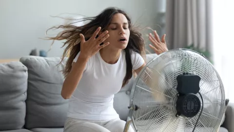 mujer con el aire del ventilador enfrente de ella, a fin de que pueda refrescarse