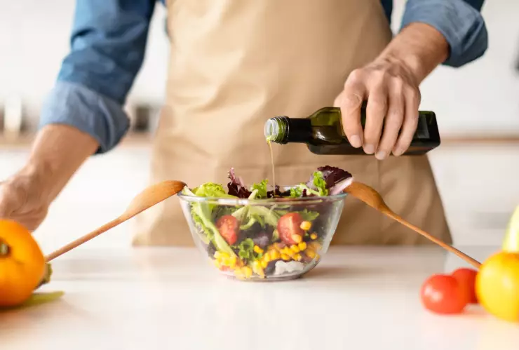 un hombre prepar&oacute; una ensalada y lo condimenta con aceite de oliva.