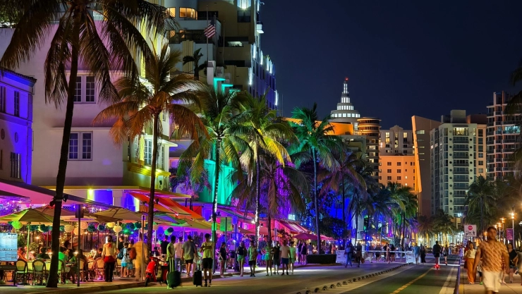 Las calles con palmeras de Miami por la noche, las luces coloridas encendidas y la gente en los bares disfrutando de un trago