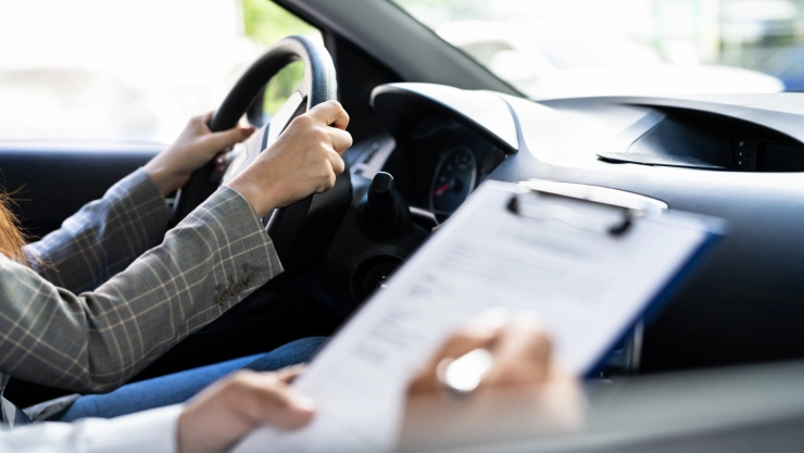 Una mujer tiene las manos al volante mientras un examinador rellena una planilla.