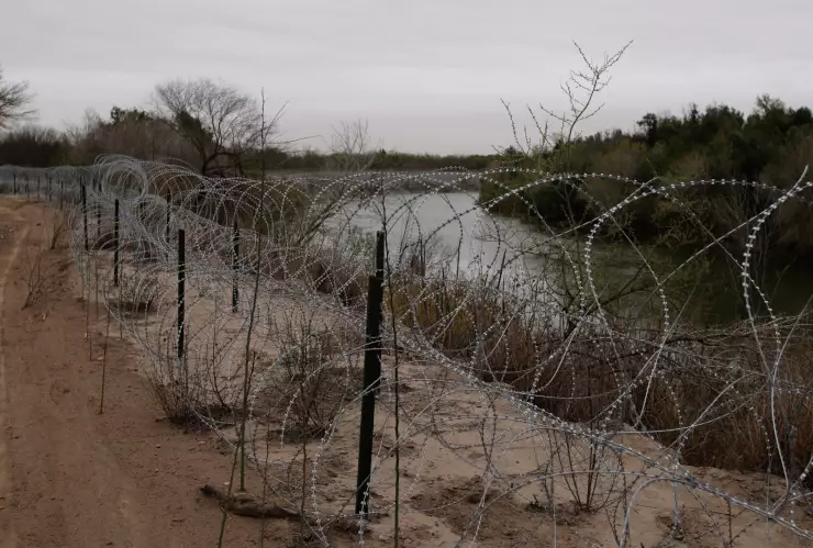 Alambre de púas que separa un territorio de tierra de otro con un río