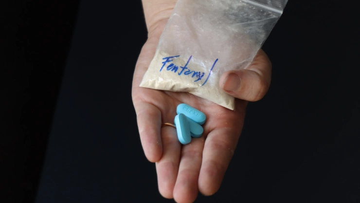 Una mano extendida con un sobre que dice “fentanilo” y tres pastillas azules