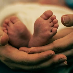 Pies de bebé sujetados por manos de adulto.