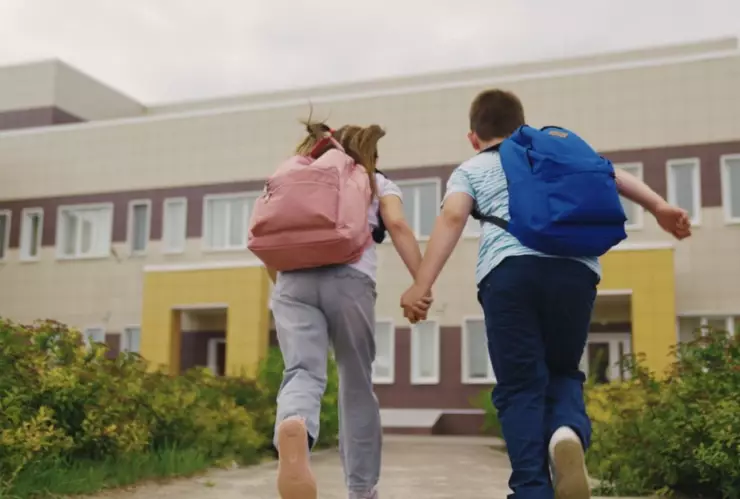 Dos niños corren hacia una escuela.