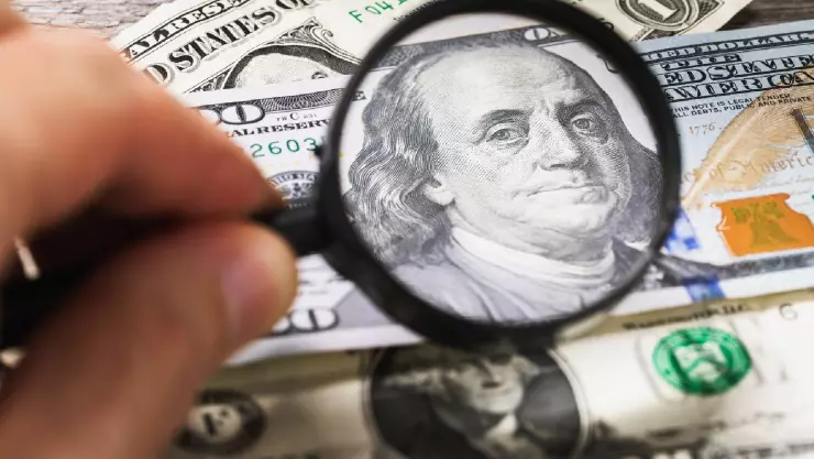 una mano con una lupa apunta a un billete de 100 dólares