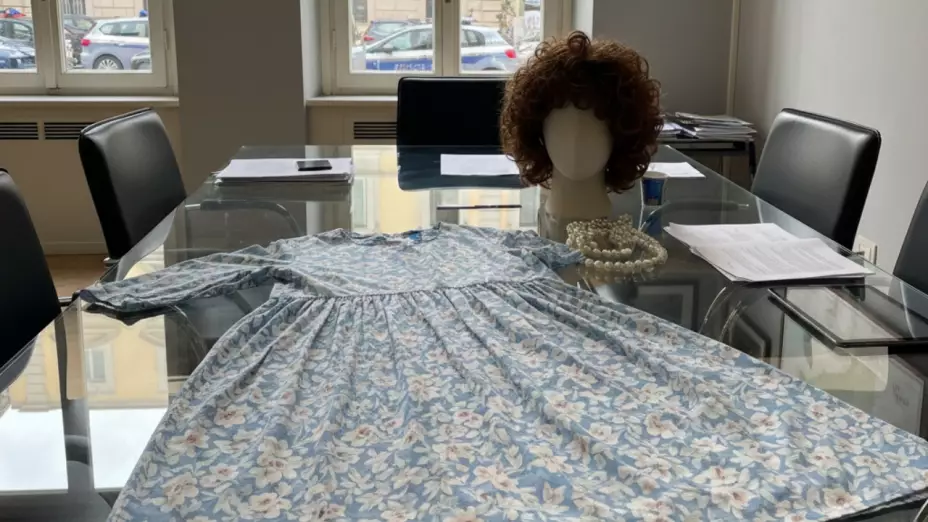 Imagen generada con Gemini AI que mustra un vestido floral, una peluca castaña sobre una mesa transparente dentro de una oficina.