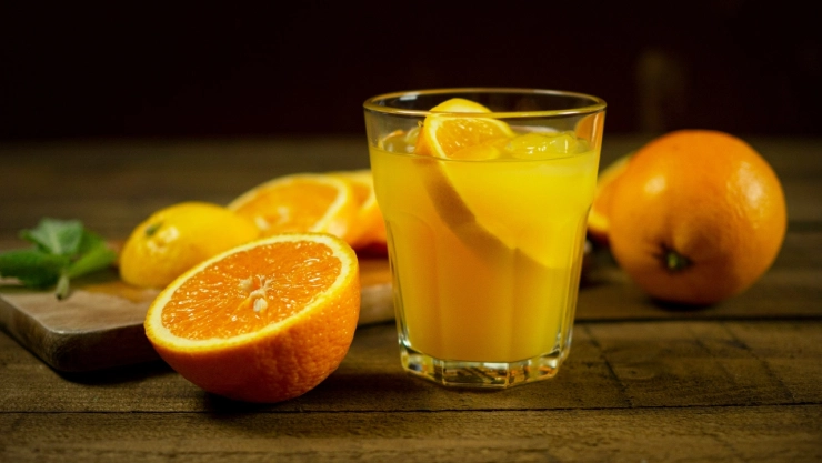 vaso de jugo con naranjas alrededor.