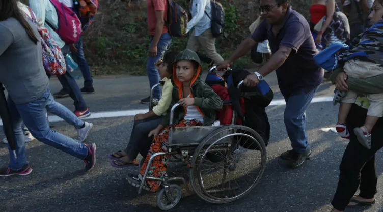 Un migrante, parte de una caravana que se dirige a la frontera entre México y Estados Unidos, empuja la silla de ruedas de un menor por la carretera en Escuintla, Chiapas, México. Imagen, AP.
