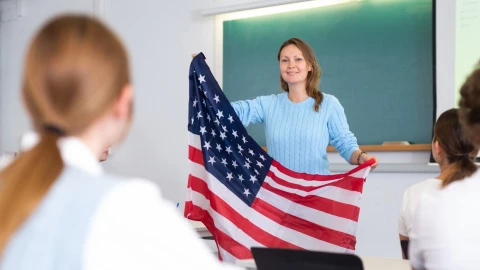 Una maestra alza una bandera de Estados Unidos al frente de los alumnos