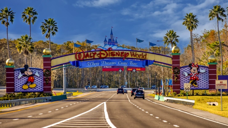 La entrada principal del parque Walt Disney World con vehículos ingresando y las palmeras de fondo