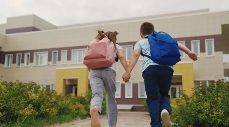 Dos niños corren hacia una escuela.