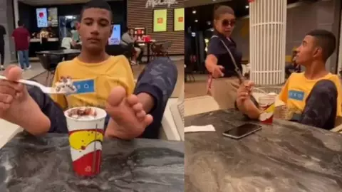 Joven sin brazos come con los pies en un centro comercial