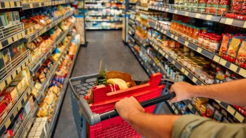 Un hombre con un coche de compra camina por un pasillo de un supermercado.