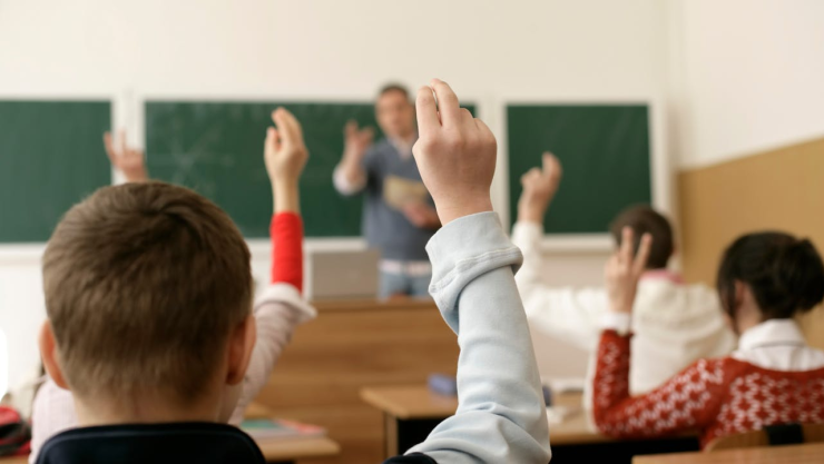 Alumnos levanta la mano, al interior de un salón de clases, para participar.