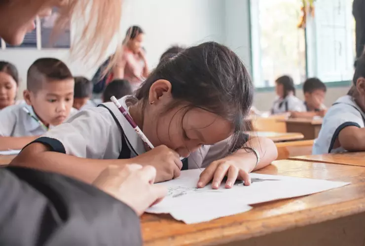 Una alumna escribiendo en su libreta en compañía de su profesora.