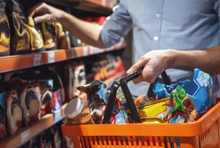 Una persona selecciona un producto en un supermercado mientras sostiene un carrito con alimentos