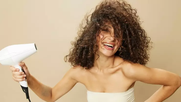 Una mujer con el cabello rizado se lo seca y sonríe felizmente