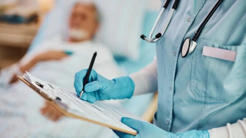 Un profesional de la salud rellena un formulario al lado de un paciente ingresado