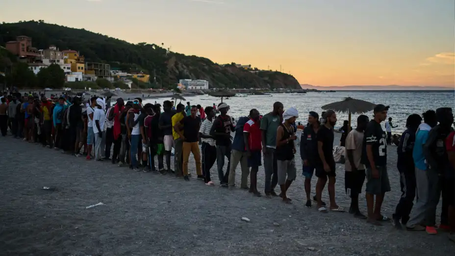 Migrantes hacen fila por comida en una playa de Ceuta, España.