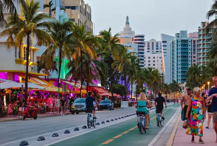 Calle costera de Miami Beach al atardecer, con gente caminando, paseando en bicicletas y disfrutando de los bares