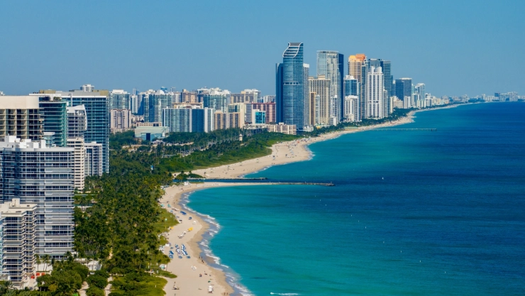 Vista aérea de las playas de Miami, con aguas turquesas, arena blanca, palmeras y grandes edificios.