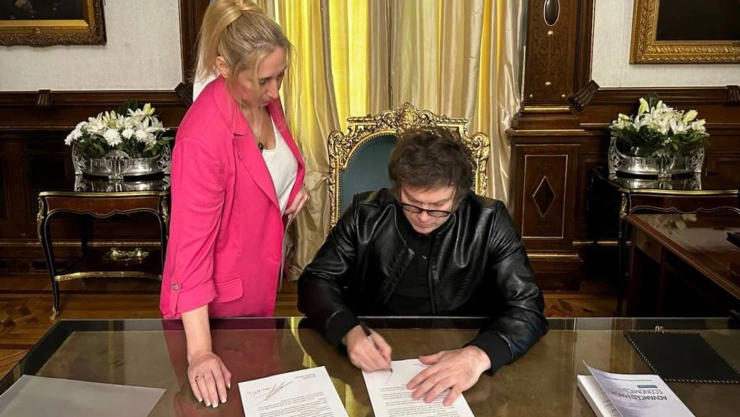 Presidente de Argentina, Javier Milei, firma documentos sobre un escritorio.