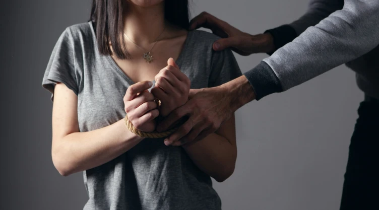 Foto de mujer sometida con lazo en las muñecas y hombre que la sujeta a un costado.