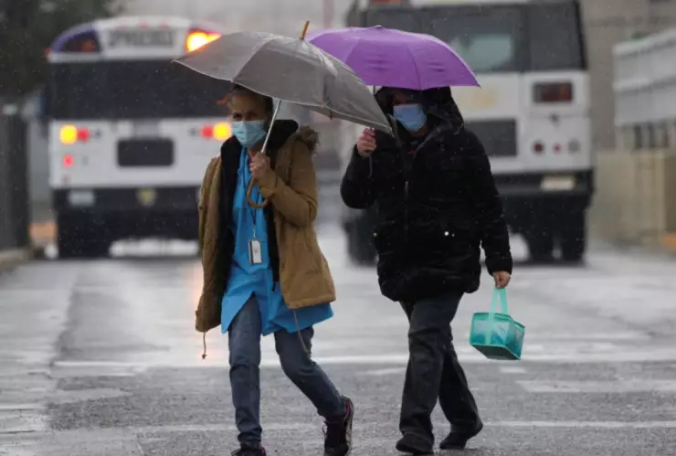 Dos mujeres muy bien abrigadas por el frío y cubriéndose con un paraguas de la lluvia.