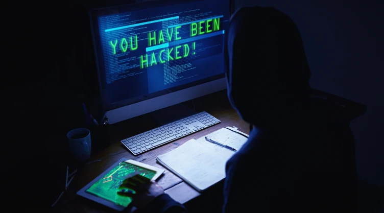 Un hacker realizando un trabajo de contraseñas, en la oscuridad, encapuchado y frente a la computadora