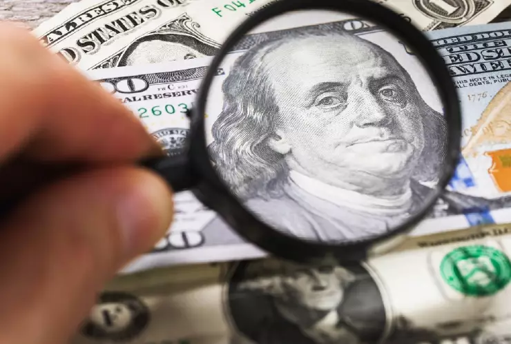 una mano con una lupa apunta a un billete de 100 dólares