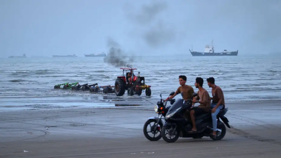 Personas en una playa mientras buques están anclados en el estrecho de Ormuz.