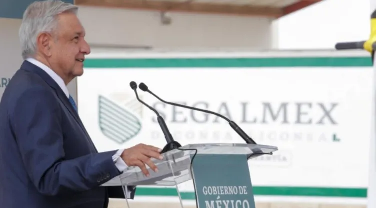 El expresidente de México, AMLO hablando por micrófono, con el logo de Segalmex de fondo.