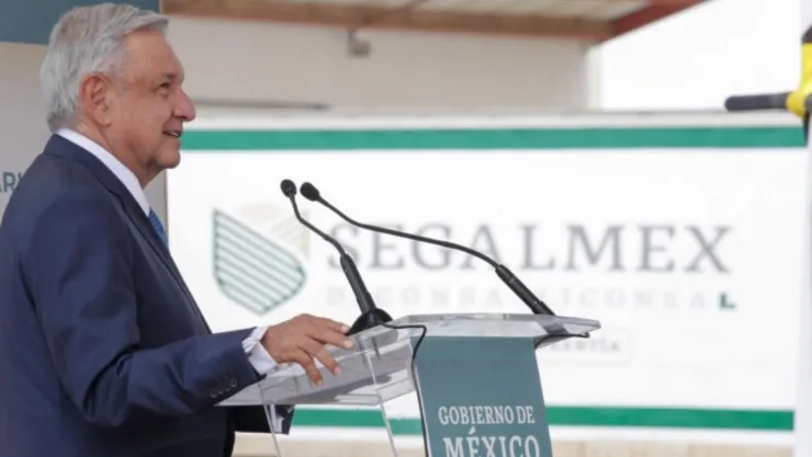 El expresidente de México, AMLO hablando por micrófono, con el logo de Segalmex de fondo.
