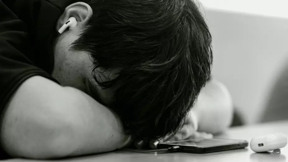 Foto de adolescente recostado sobre mesa con teléfono celular.