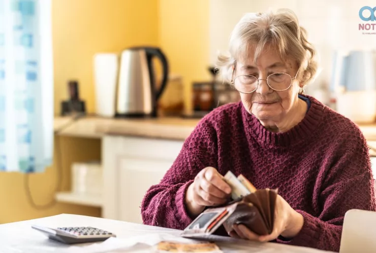 Una mujer mayor sacando billetes de su cartera.