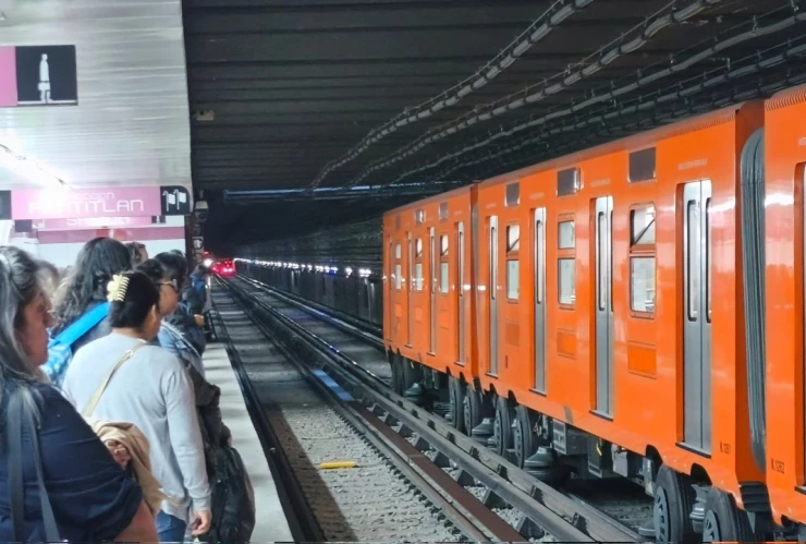 Estación de la Línea 1 del Metro CDMX con tren en andén y personas en el pasillo.