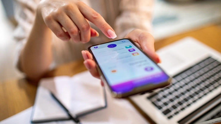 una mujer monitorea sus cuentas desde el teléfono y la computadora.
