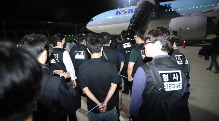 Agentes de la policía surcoreana escoltan a ciudadanos surcoreanos sospechosos de participar en estafas en línea antes de abordar un avión de Korean Air en el Aeropuerto Internacional de Techo, provincia de Kandal, Camboya, el 18 de octubre de 2025.