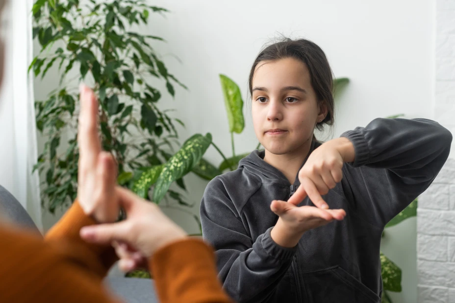 Cute little girl make hand gesture learning sign language with mom or female nanny, smiling small kid practice nonverbal talk with teacher at home, preschooler disabled child have lesson with tutor