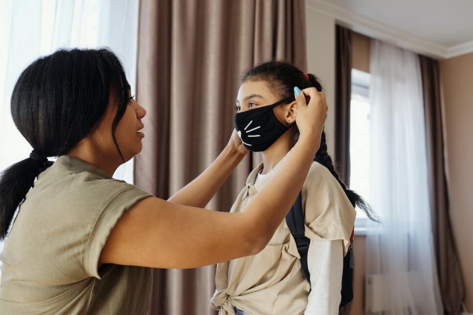 madre colocando cubrebocas a su hija sin vacunar
